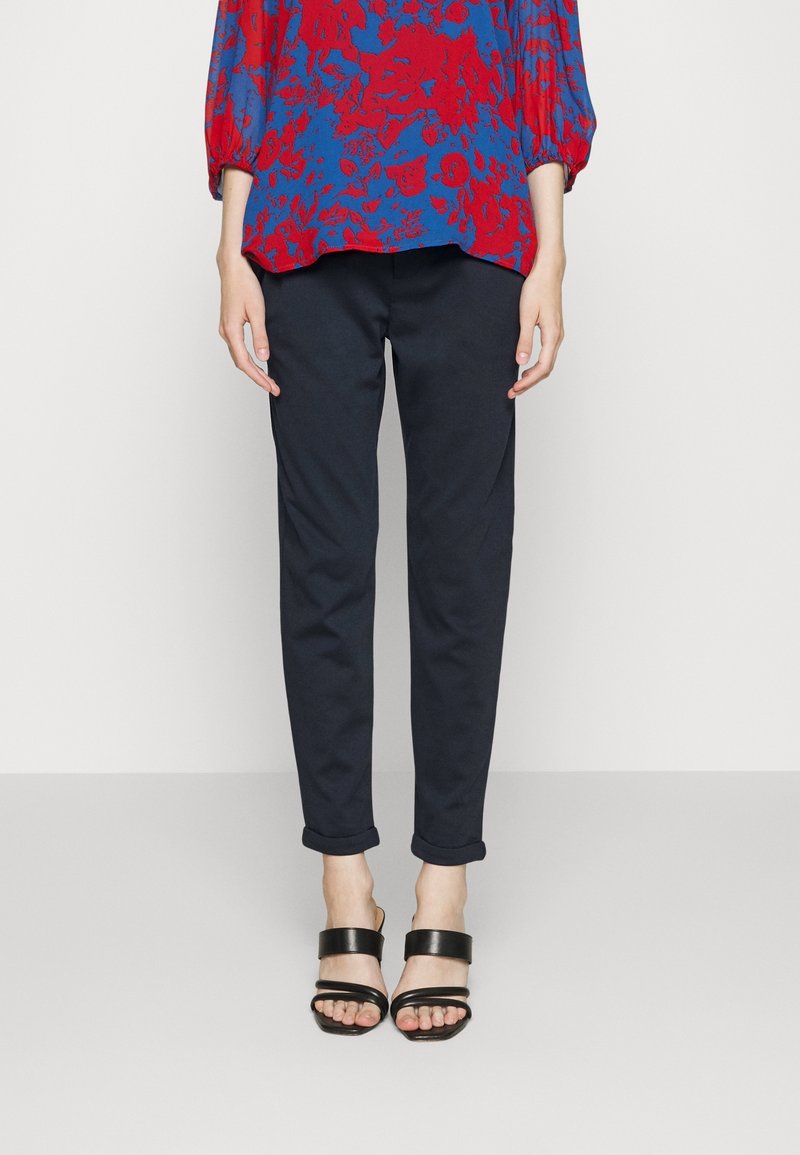 Marina smala byxor med uppvikta fållar, i kombination med svarta sandaler med breda remmar. Överdel med ett mönster av röda och blå blommor.