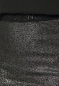 Black elastic waistband with "CALVIN KLEIN JEANS" branding above a shimmery gray fabric with a smooth, metallic texture.