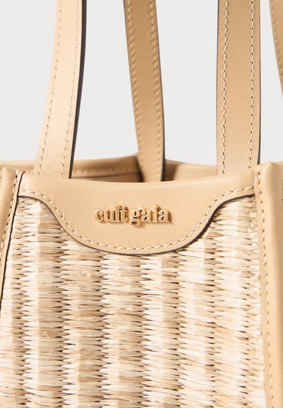 Borsa tote in paglia intrecciata beige con parte superiore in pelle liscia, manici corti e una placca logo dorata. Esterno testurizzato con un motivo distintivo.