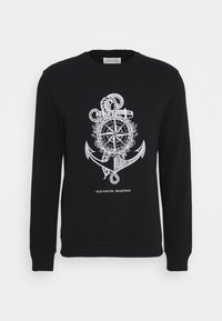 Sweatshirt noir présentant un motif nautique blanc avec une ancre, une boussole et une corde. Comprend le texte « OLD SAILOR TRADITION » sous le dessin.