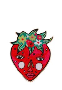 Broche en forme de fraise avec un fond rouge, comportant un visage, des feuilles vertes sur le dessus et des accents floraux colorés. Fini texturé et brillant.