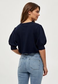 Tmavě modrý pletený top s krátkými nabíranými rukávy, kulatým výstřihem a žebrovanými manžetami; nošený s světle modrými slim fit džíny.