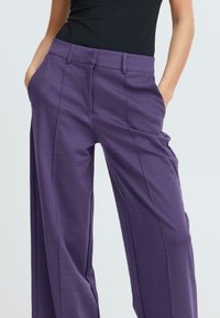 Pantalons larges violets avec une texture lisse, dotés de plis avant et de poches latérales. Conçus avec une coupe décontractée et une taille ajustée.