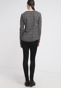 Top gris de manga larga con estampado combinado con leggings negros ajustados; modelo visto de espaldas, mostrando la silueta y la textura de las telas.