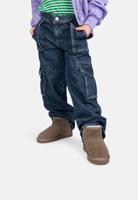 Denim cargo broek met meerdere zakken, knoopsluiting en een relaxte pasvorm, gecombineerd met bruin suede enkelboots met een zachte binnenvoering.