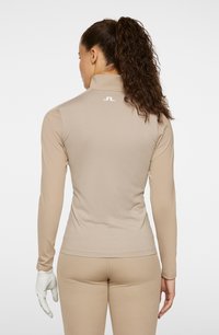 Beige långärmad topp med en figurnära design, texturerad tyg och hög krage. Har en vit logotyp på ryggen.