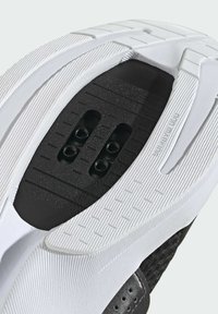 Semelle de chaussure de sport en noir et blanc avec un caoutchouc texturé, de multiples motifs d'adhérence et trois trous d'attache pour des crampons. Matériau non marquant.