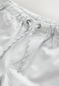 Shorts de bain gris clair avec une taille élastique, dotés d'un cordon blanc avec des accent noir et de subtils détails de couture.