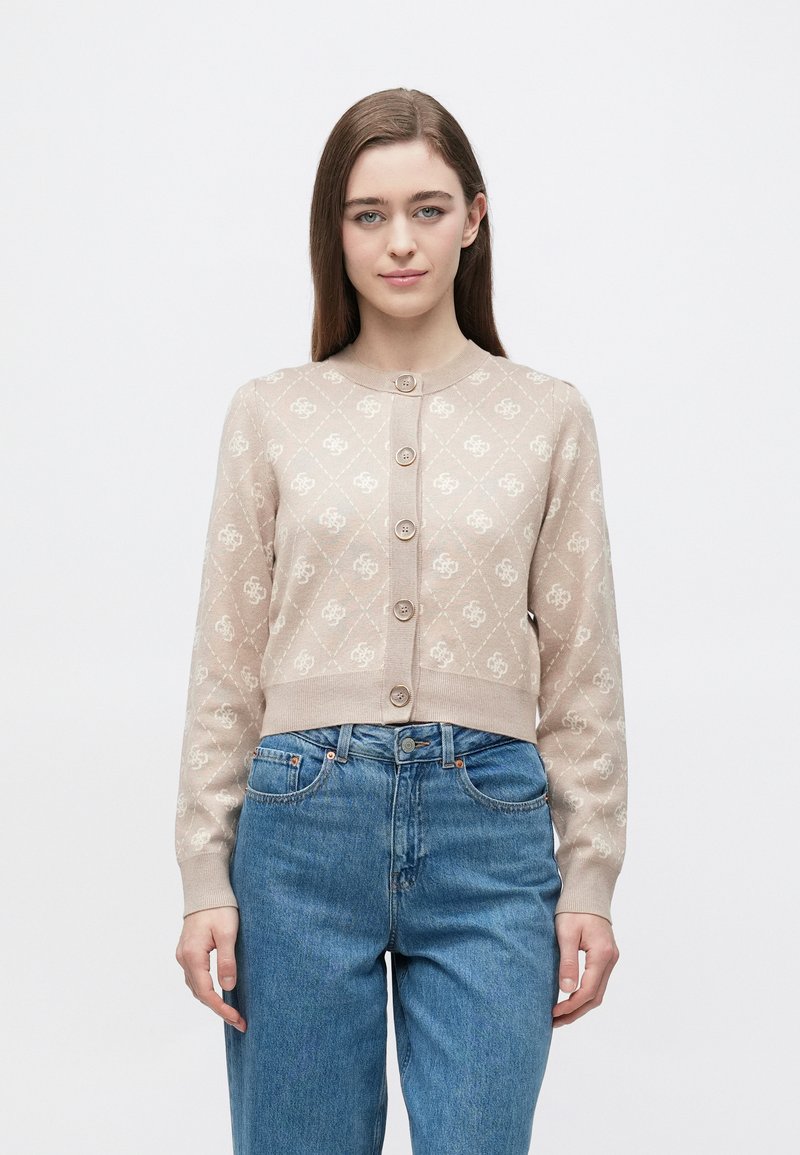 Μπεζ πλεκτή ζακέτα με διαμαντένιο μοτίβο, στρογγυλή λαιμόκοψη, εμπρός με κουμπιά και μακριά μανίκια. Συνδυασμένη με μπλε τζιν ψηλόμεσα παντελόνια.