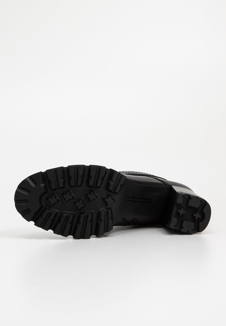 Bottines noires avec semelle en caoutchouc, présentant un motif de crantage texturé. La tige est en matériau lisse avec des coutures renforcées pour une durabilité accrue.