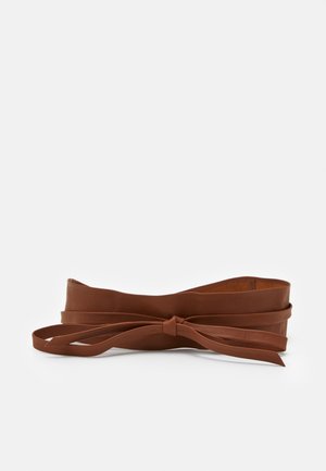 Ceinture en cuir marron avec une large bande et un nœud papillon noué à l'avant sur un fond blanc uni.