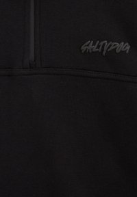 Melns flīsa džemperis ar ceturtdaļas rāvējslēdzēju un iepotētu "SALTYDOG" logotipu uz krūts, ar gludu, mīkstu tekstūru.