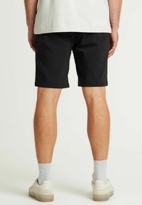 Zwarte shorts met een gladde textuur, knielange ontwerp. Gecombineerd met lichtgrijze sokken en casual sneakers, gezien vanuit de achterkant.