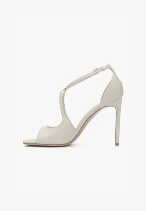 Beige leren sandaal met hoge hak, open teen, dunne enkelriem en stilettohak, zijaanzicht op een witte achtergrond.