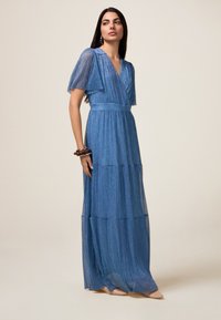 Rochie maxi albastră cu design stratificat și pliat, mâneci scurte și decolteu în formă de V. Realizată dintr-un material strălucitor și texturat. Detaliu neted la talie.