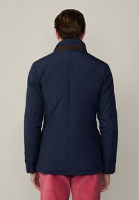 Giacca trapuntata blu navy con colletto alto, caratterizzata da accenti marroni e una vestibilità su misura. Texture liscia con una superficie a motivo a diamante.