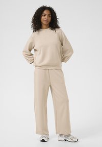 Beige sweat top with long sleeves and elastic cuffs, paired with matching wide-leg sweatpants. Soft fabric, relaxed fit, minimal design.