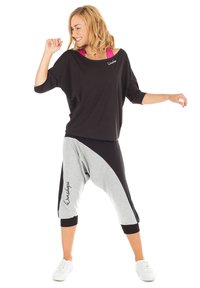 Top negro de gran tamaño con un escote ancho, combinado con pantalones estilo harem en gris y negro que presentan un diseño diagonal y un logotipo. Zapatillas blancas.