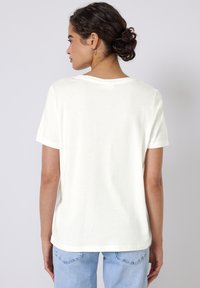 T-shirt crème à manches courtes avec un col rond et une coupe décontractée, fabriqué en coton doux, avec un design uni sans motifs.