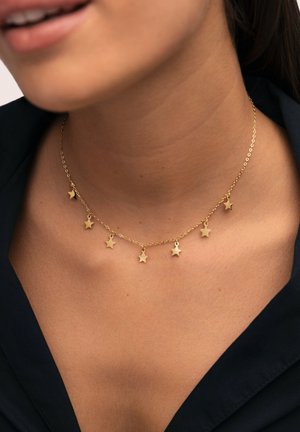 Collar con colgante de estrella dorada y una cadena delicada, con pequeños colgantes en forma de estrella, espaciados uniformemente, llevado sobre una tela oscura.