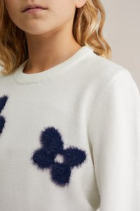 Valkoinen neulepusero, jossa on kolme tummansinistä pörröistä kukka-applikaatiota. Pyöreä pääntie, jossa ribbikuitu hihansuissa ja helmassa, teksturoitu kangas.