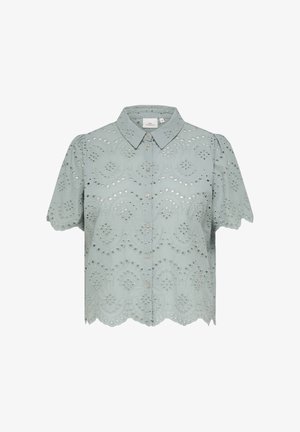Blouse bleu clair à manches courtes, boutonnée sur le devant, avec un ourlet festonné et des motifs de broderie ajourée sur toute la surface.