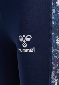 Marina atletiska leggings med blommiga sidopaneler, med en vit "hummel"-logotyp fram. Materialet är mjukt och elastiskt.