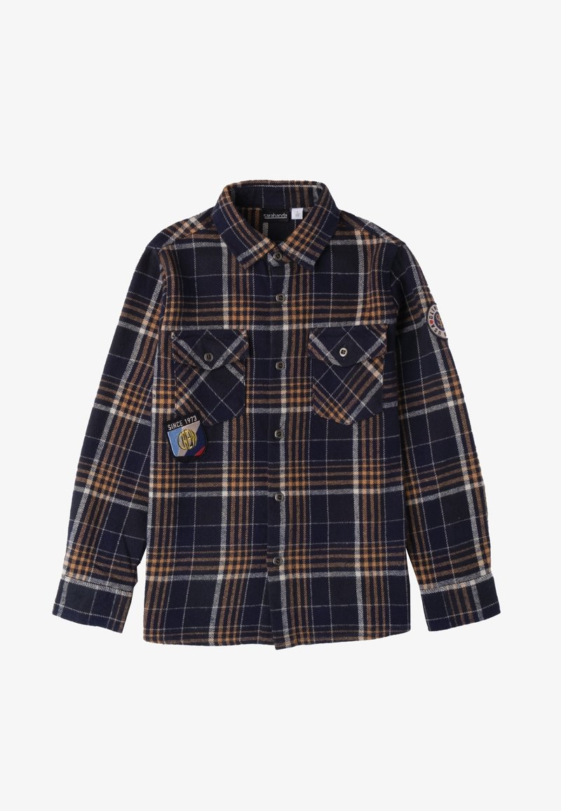 Camicia in flanella a quadri blu navy e marrone con bottoni davanti, due tasche sul petto e un distintivo sulla tasca sinistra. Maniche lunghe con polsini abbottonati.