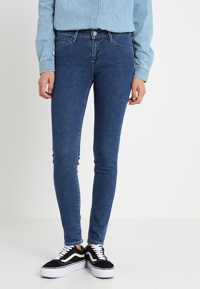 Jean skinny en denim bleu foncé, avec une taille haute, une coupe slim, cinq poches et une fermeture à bouton. Associé à des baskets noires et blanches.