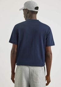 T-shirt in cotone blu navy con maniche corte, scollo a rotondo e vestibilità rilassata, abbinato a pantaloni corti grigi chiari. La vista posteriore mostra un design semplice.