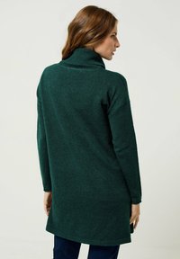 Maglione verde a collo alto in knit con maniche lunghe, vestibilità rilassata e spacchi laterali. Tessuto testurizzato con dettagli raffinati sul colletto e sull'orlo.
