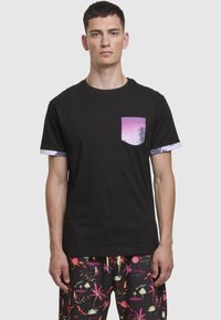 Juoda medvilninė marškinėliai su violetinės ir rožinės spalvos kišene, kurioje pavaizduotas palmės medis. Trumpomis rankovėmis su kontrastingais mėlynais akcentais.