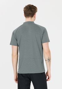 Grå kortärmad idrottströja med ett texturerat mönster och ståkrage. Har en avslappnad passform och en bakre etikett för enkel användning.