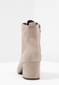 Botas de tobillo de ante beige con un tacón bloque de altura media, que presentan un cierre lateral con cremallera y una textura suave.