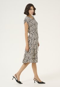 Robe à motifs noir et blanc avec des manches courtes, taille cintrée et jupe évasée. Associée à des escarpins à talons ouverts noirs. Texture de tissu lisse.