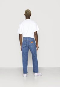 Modré džíny z denimu se střihy přímo dole, s hnědou koženou nášivkou na zadním pásku a dvěma zadními kapsami. Kombinované s bílým tričkem.