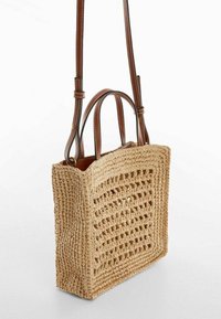 Sac en paille tressée de forme rectangulaire ; possède des poignées en cuir marron et un motif de tissage ouvert pour la ventilation. Couleur beige clair.