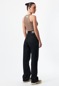 Brown ribbed tank top paired with black high-waisted, wide-leg pants. Notable back pockets and a brand label on the waistband. Casual footwear.