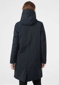 Tmavě modrý nepromokavý kabát s vysokým límcem a kapucí, který se vyznačuje elegantním designem, dlouhými rukávy a rozvorem na zádech pro volnost pohybu.