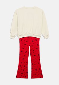 Κρεμ φούτερ με μακριά μανίκια συνδυασμένο με κόκκινο καμπάνες παντελόνι με διασκορπισμένα σχέδια μαύρης κερασιάς και καρδιές.