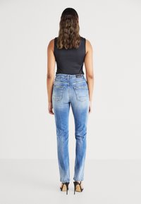 Sinine denim materjalist teksad, millel on pleekinud värv, sirge sääre disain ja taskud. Kombineeritud musta varrukateta särgi ja kõrgete kontsadega.