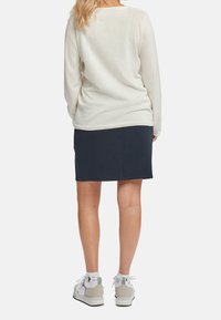 Pull crème clair à manches longues associé à une jupe bleu marine foncé. La tenue présente une coupe décontractée et une texture douce, complétée par des baskets grises.