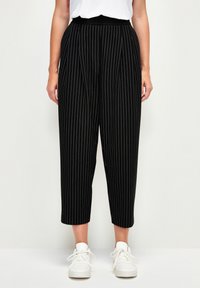Pantalons à rayures noires et blanches avec une taille élastique haute, longueur courte et coupe décontractée, portés avec des baskets blanches.