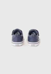 Námořnické modré kožené tenisky s bílou gumovou podrážkou, vybavené suchým zipem a brandingem "Converse All Star" na patě.
