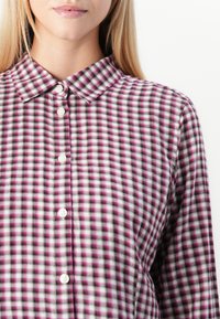 Checkered button-up shirt featuring a classic collar. Fabric displays pink, white, and purple hues with a soft texture. Five white buttons.