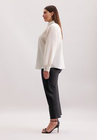 Blusa bianca con colletto, texture a costine, maniche lunghe e polsini con bottoni abbinata a pantaloni neri a gamba dritta e tacchi a cinturino neri.