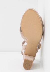Sandale beige en suède avec talon bloc vue par le dessous, mettant en avant la semelle lisse et le protège-talons en caoutchouc antidérapant.
