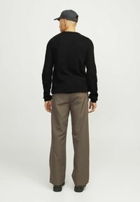 Maglione a coste nero con scollo tondo, abbinato a pantaloni taupe larghi e scarpe nere, visto da dietro.
