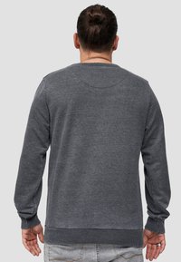 Grijze sweater met lange mouwen, geribbelde manchetten en onderkant, met een gladde textuur en een ronde halslijn. Eenvoudig, onopvallend ontwerp.