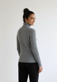 Szary prążkowany sweter z golfem, długimi rękawami, o dopasowanym kroju i miękkiej teksturze. Noszony z czarnymi spodniami, podkreślającymi design swetra.